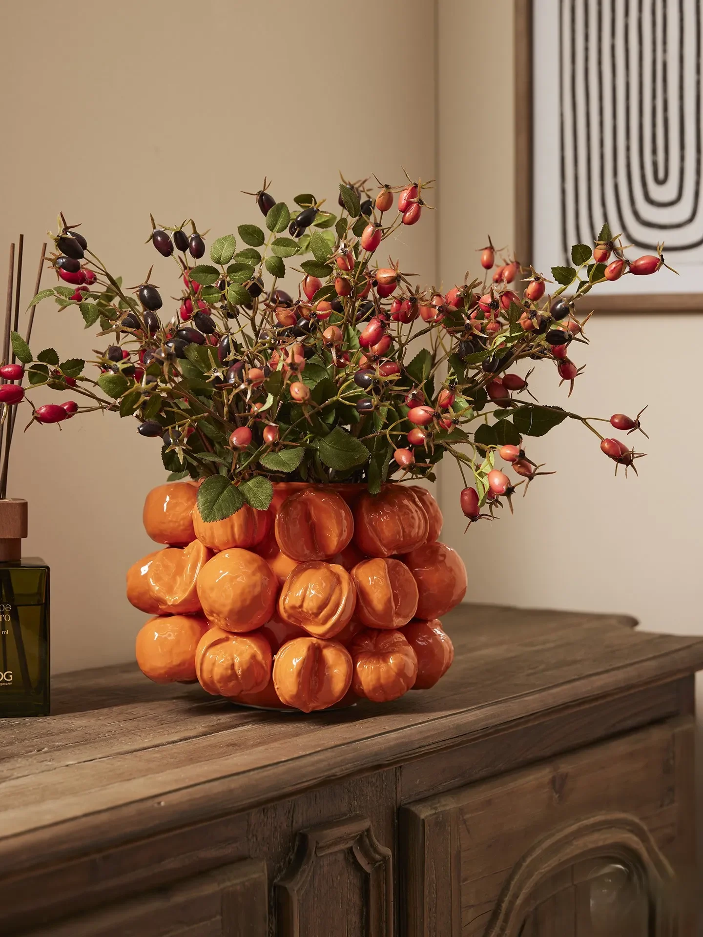 A decorative vase filled with pink and dark purple berries and green leaves, resting on a wooden surface.