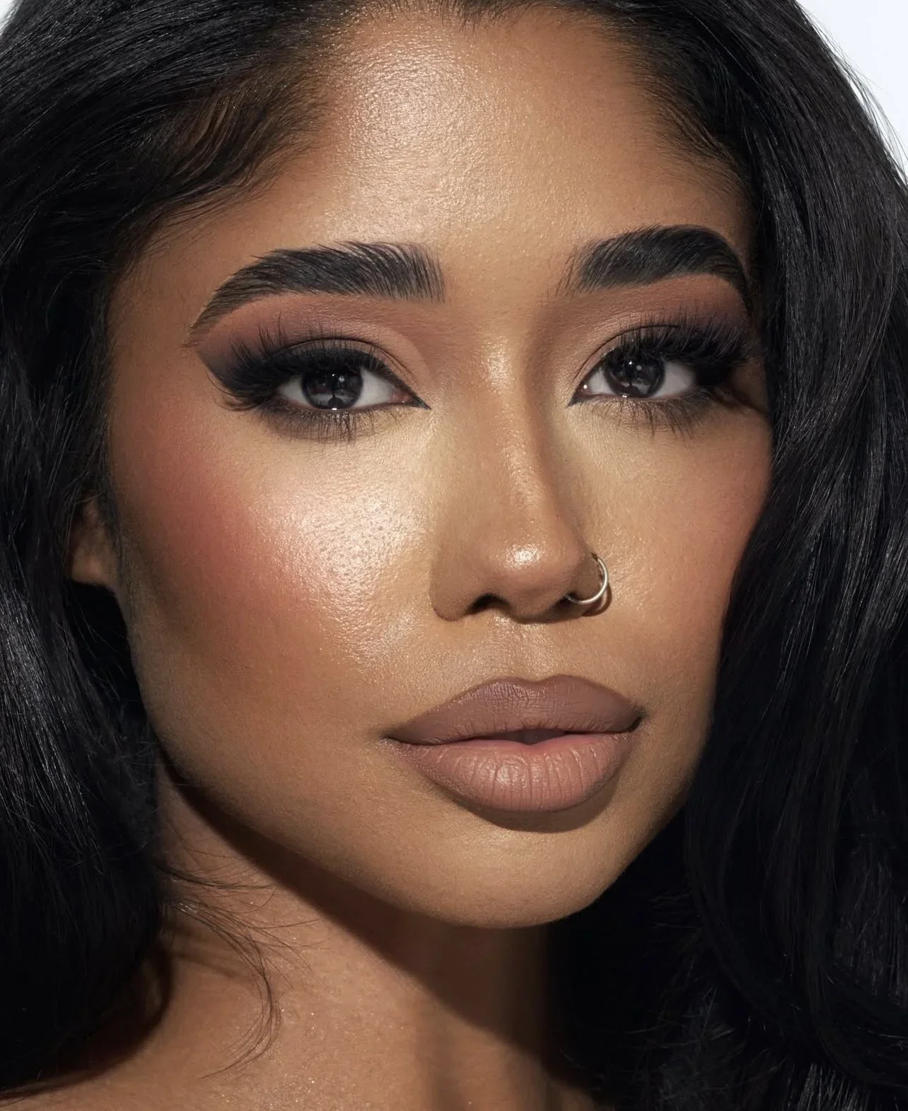 Close-up of a woman's face with detailed makeup, dark hair, and a septum piercing.