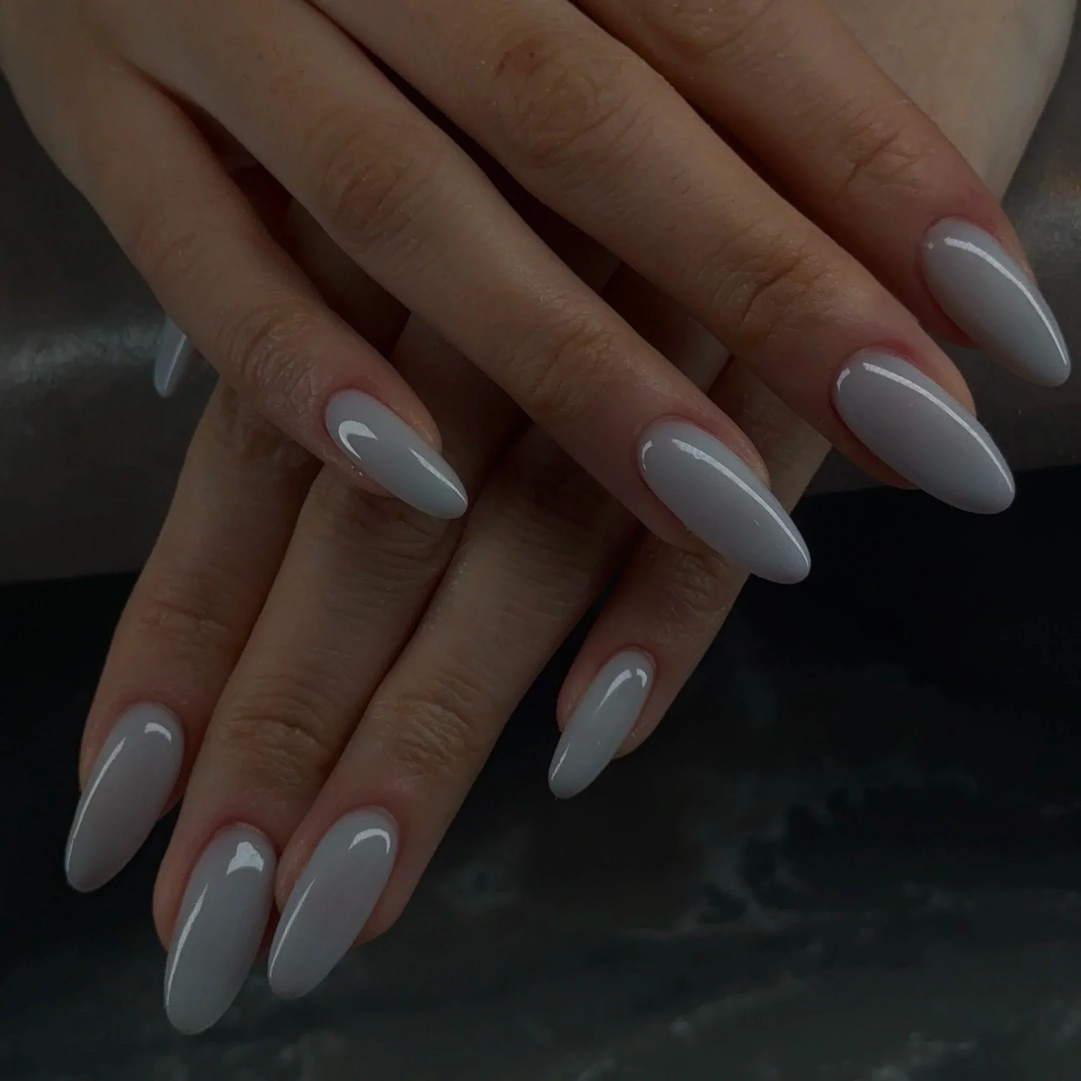 Close-up of a person's hand with nails painted in a light color and fingers overlapping a dark surface.