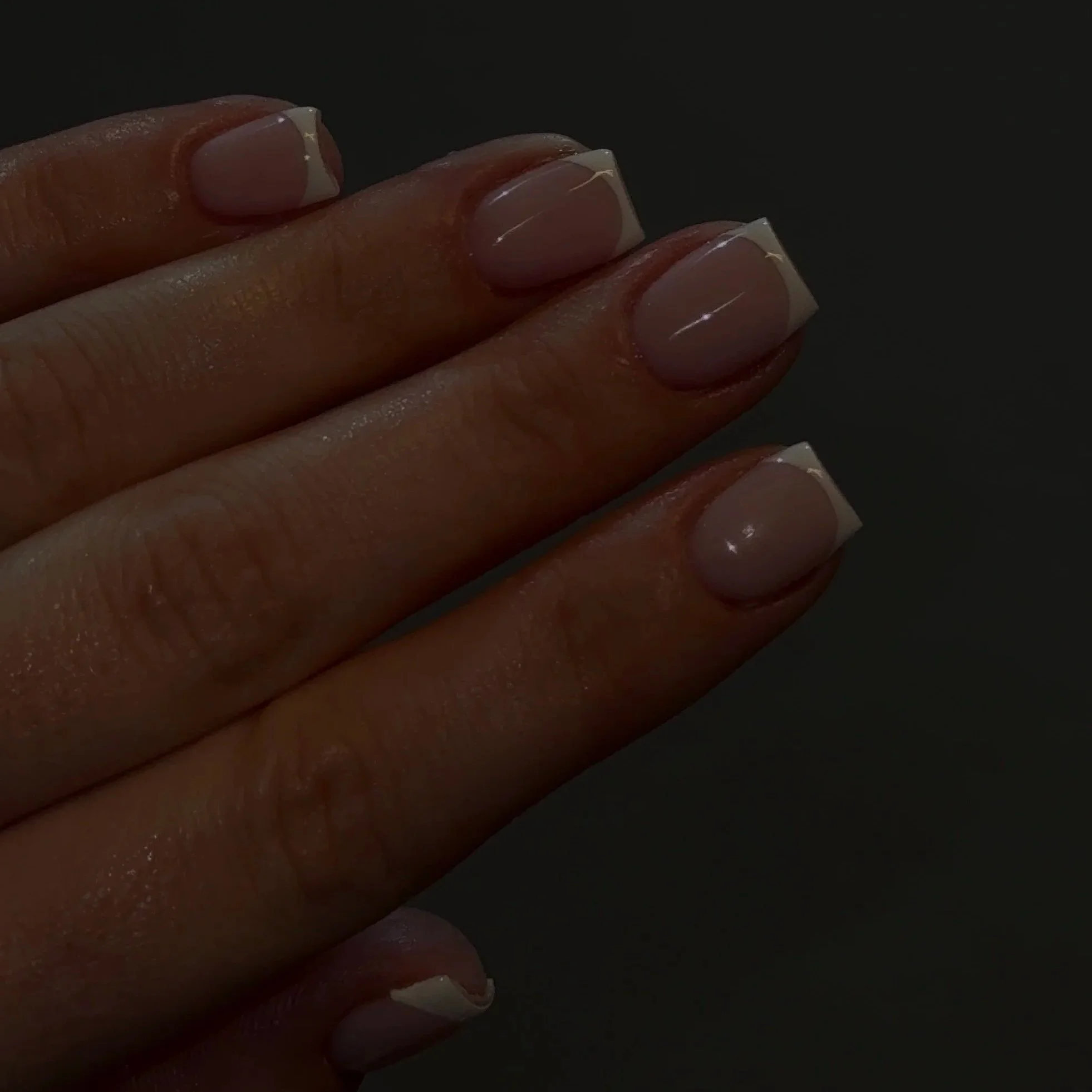 Close-up of a hand with nails painted in French manicure style against a dark background.