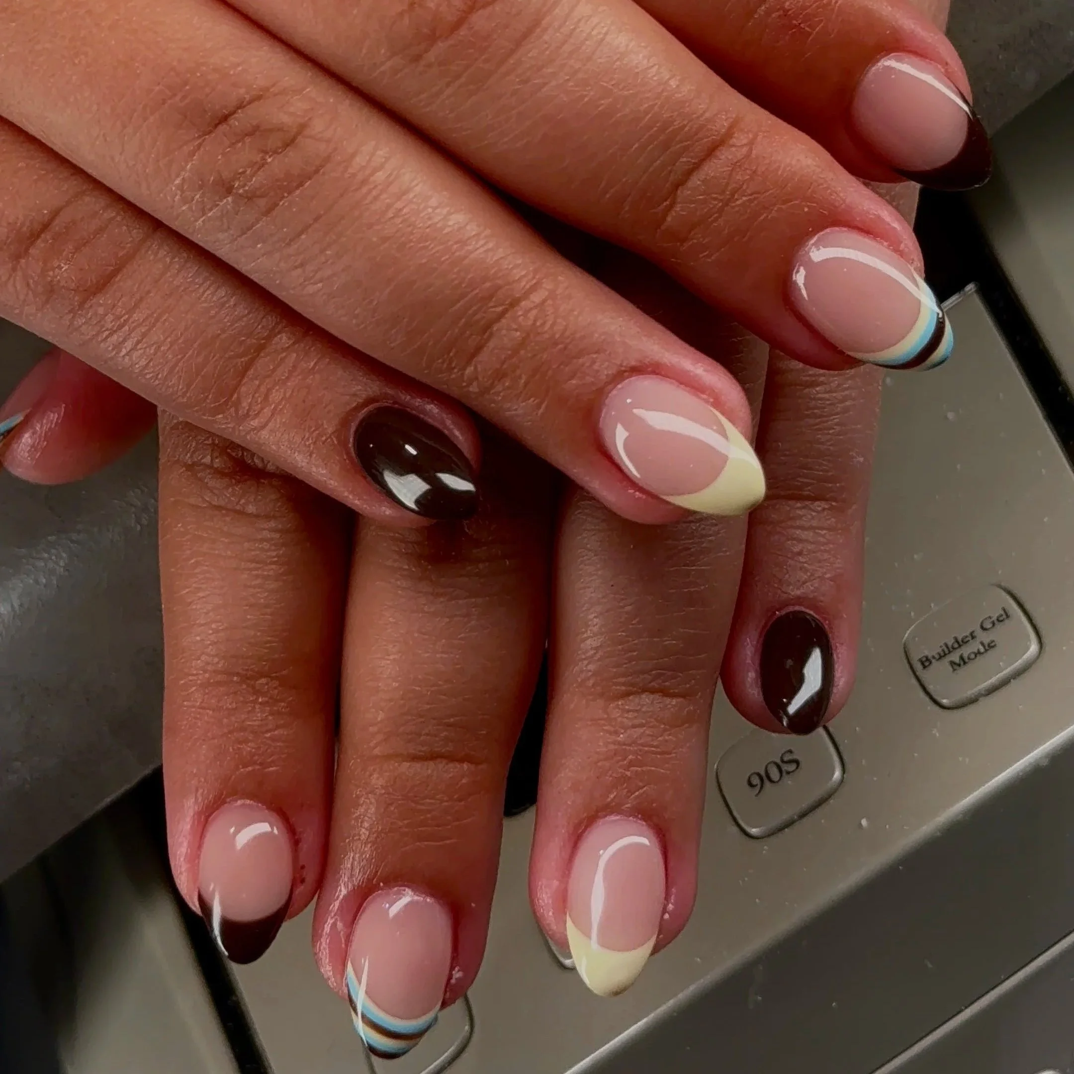Close-up of a person's hand with manicured nails featuring a French tip design with colorful accents and dark polish on one finger, resting on a keypad.