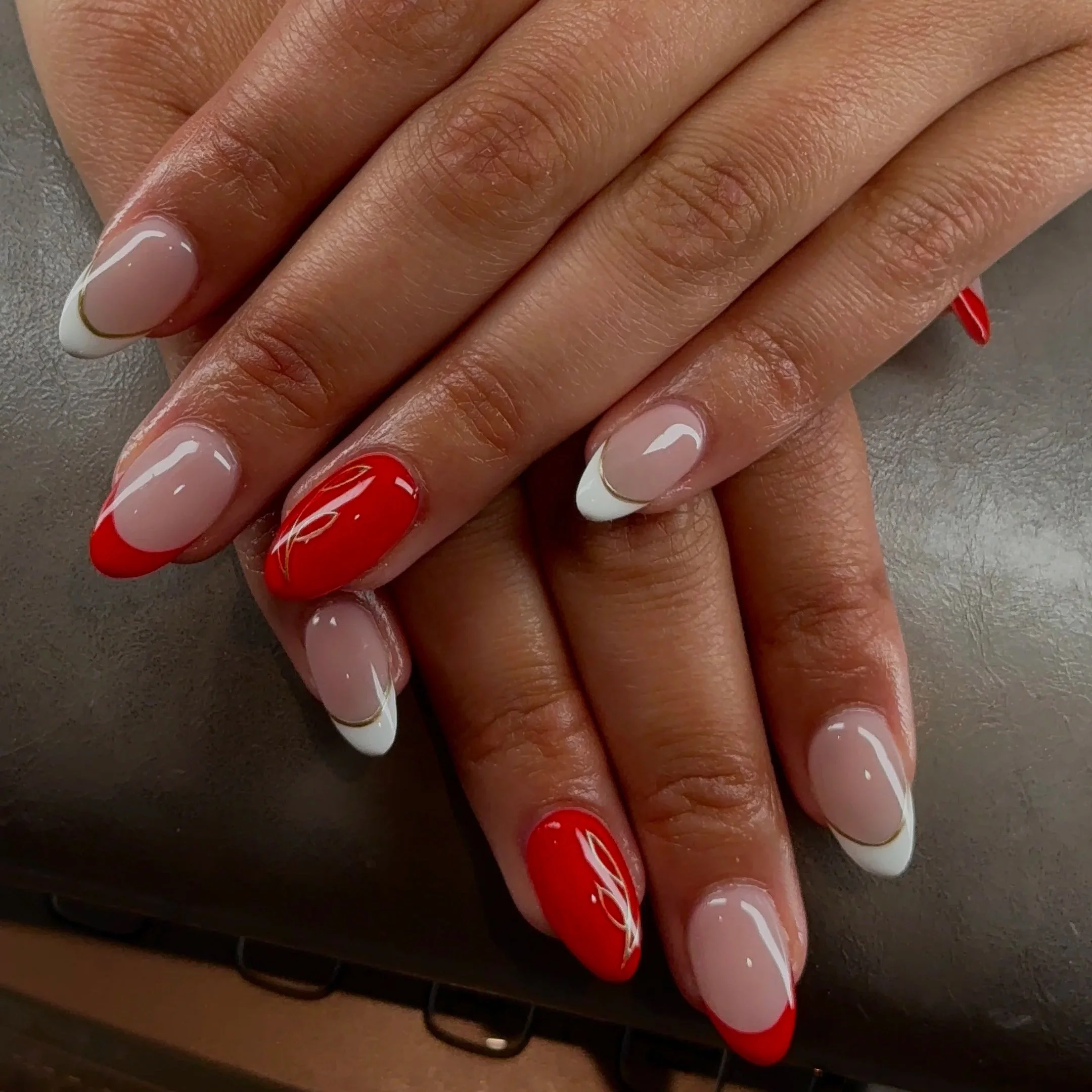 Close-up of hands with manicured nails, featuring red, white, and pink nail polish with decorative lines and patterns.