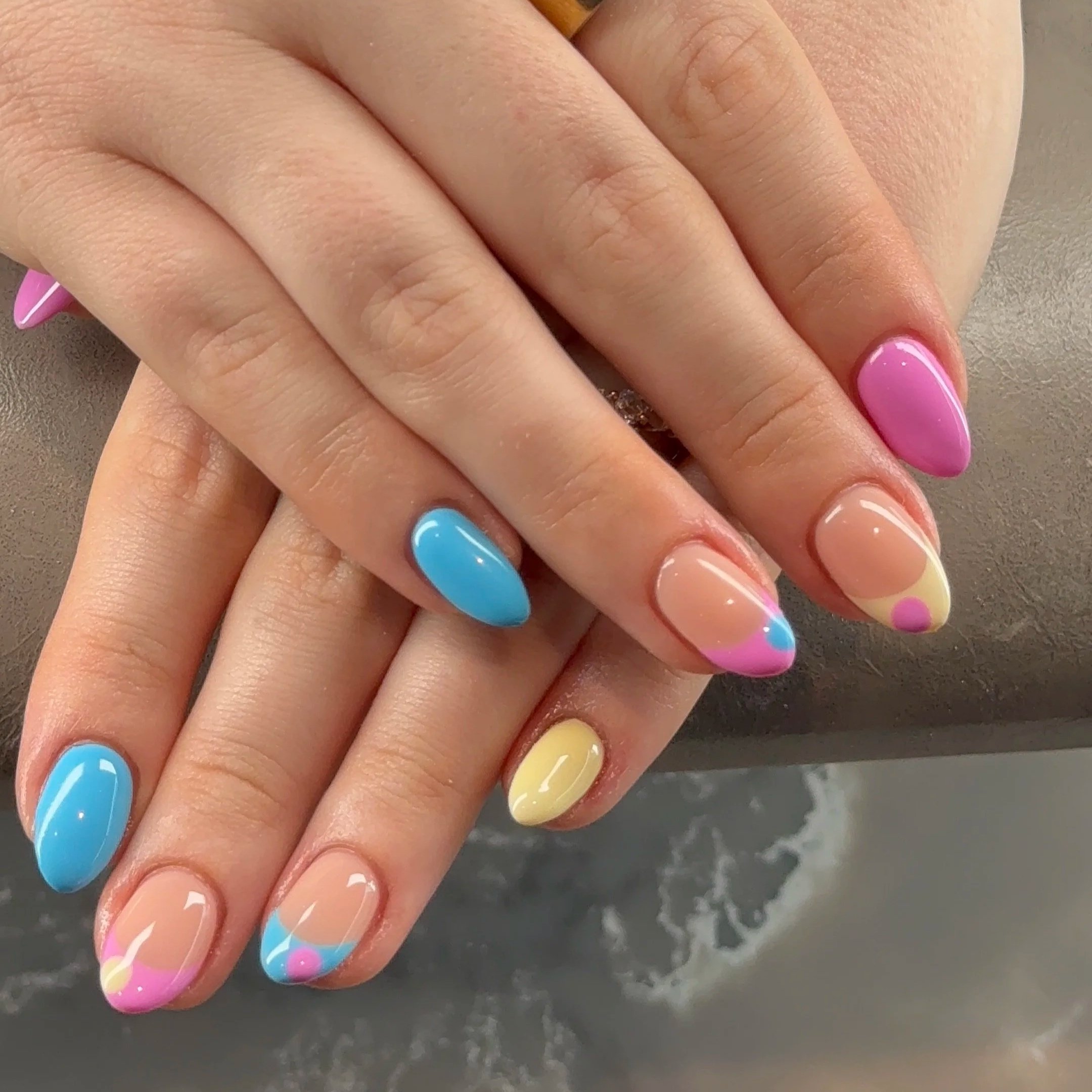 Close-up of a hand with multicolored pastel nail polish, featuring pink, yellow, blue, and peach nails.