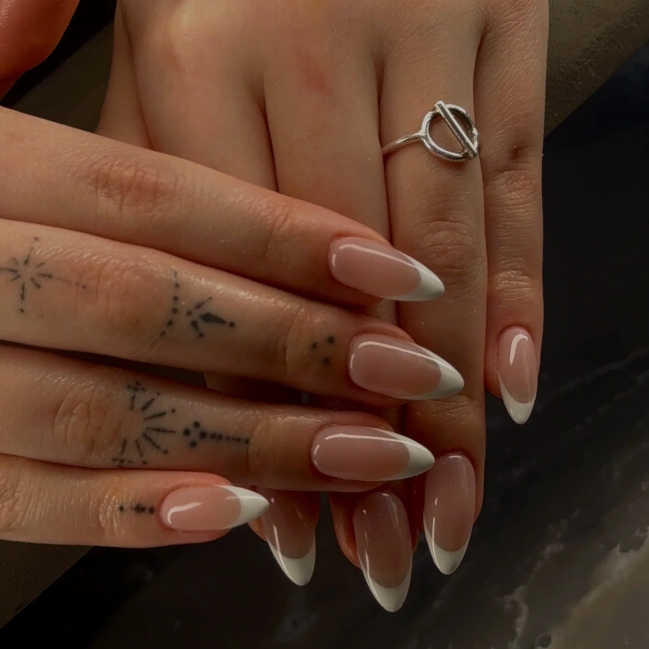 Close-up of a person's hand with floral tattoos, wearing a silver ring and manicured nails with French tips.