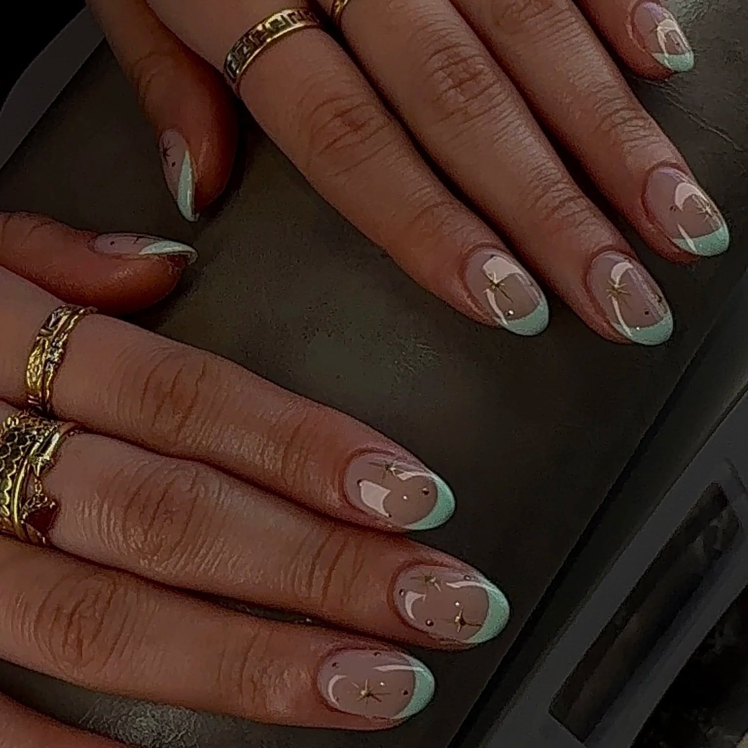 Close-up of hands with decorated nails featuring a panda and palm tree design, wearing rings, resting on a dark surface.