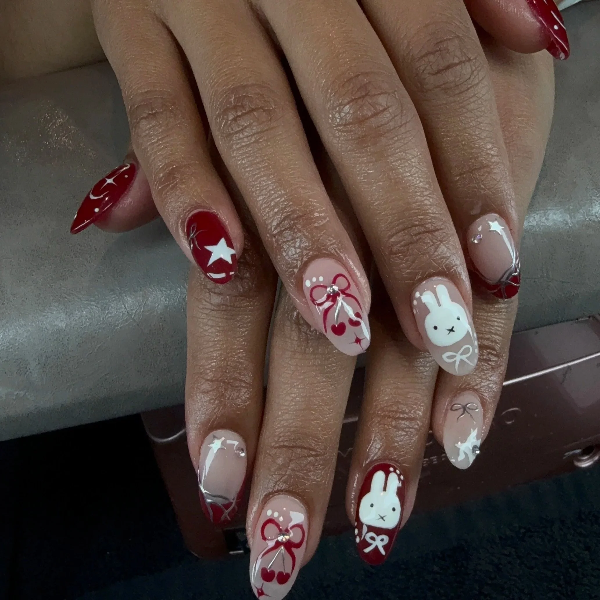 Close-up of a hand with decorated nails featuring red, white, and pink Christmas-themed designs including stars, bows, and a bear face.