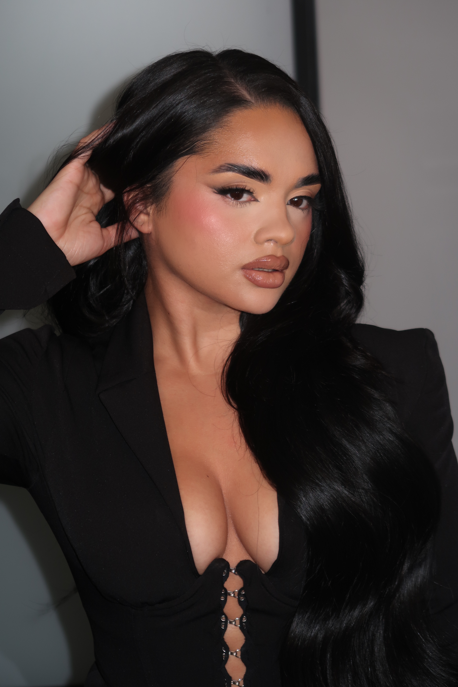 A woman with long black hair and makeup looking at the camera, dressed in a black top with a lace-up front detail.