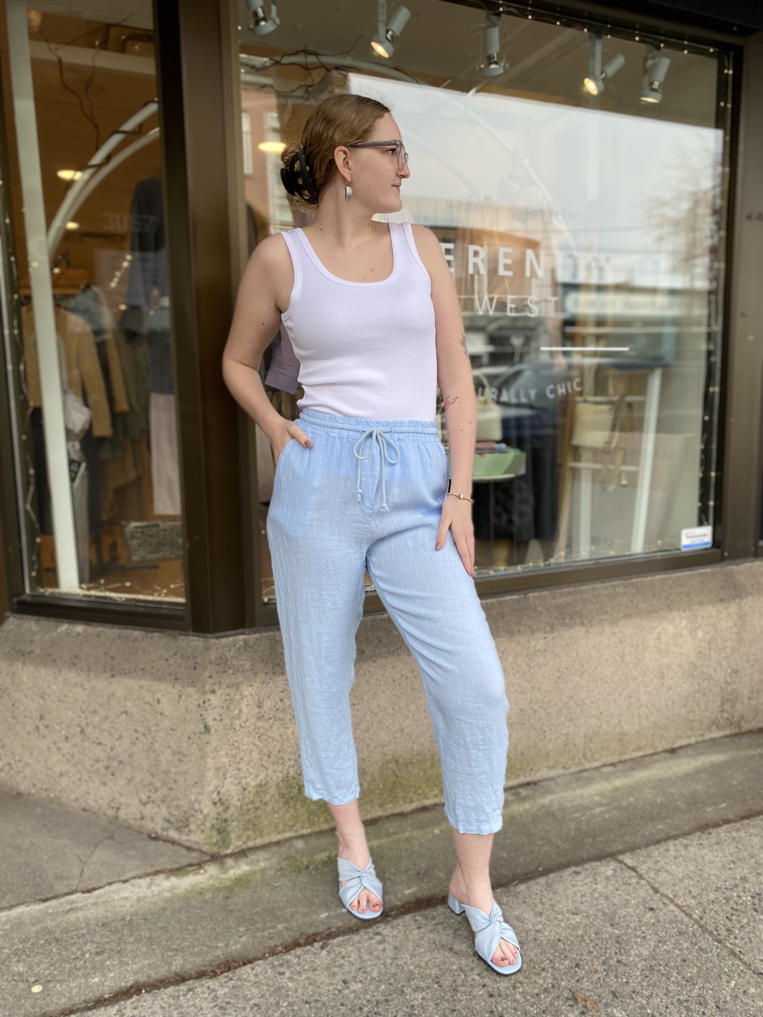 Person in front of a storefront wearing a white tank top and light blue pants.
