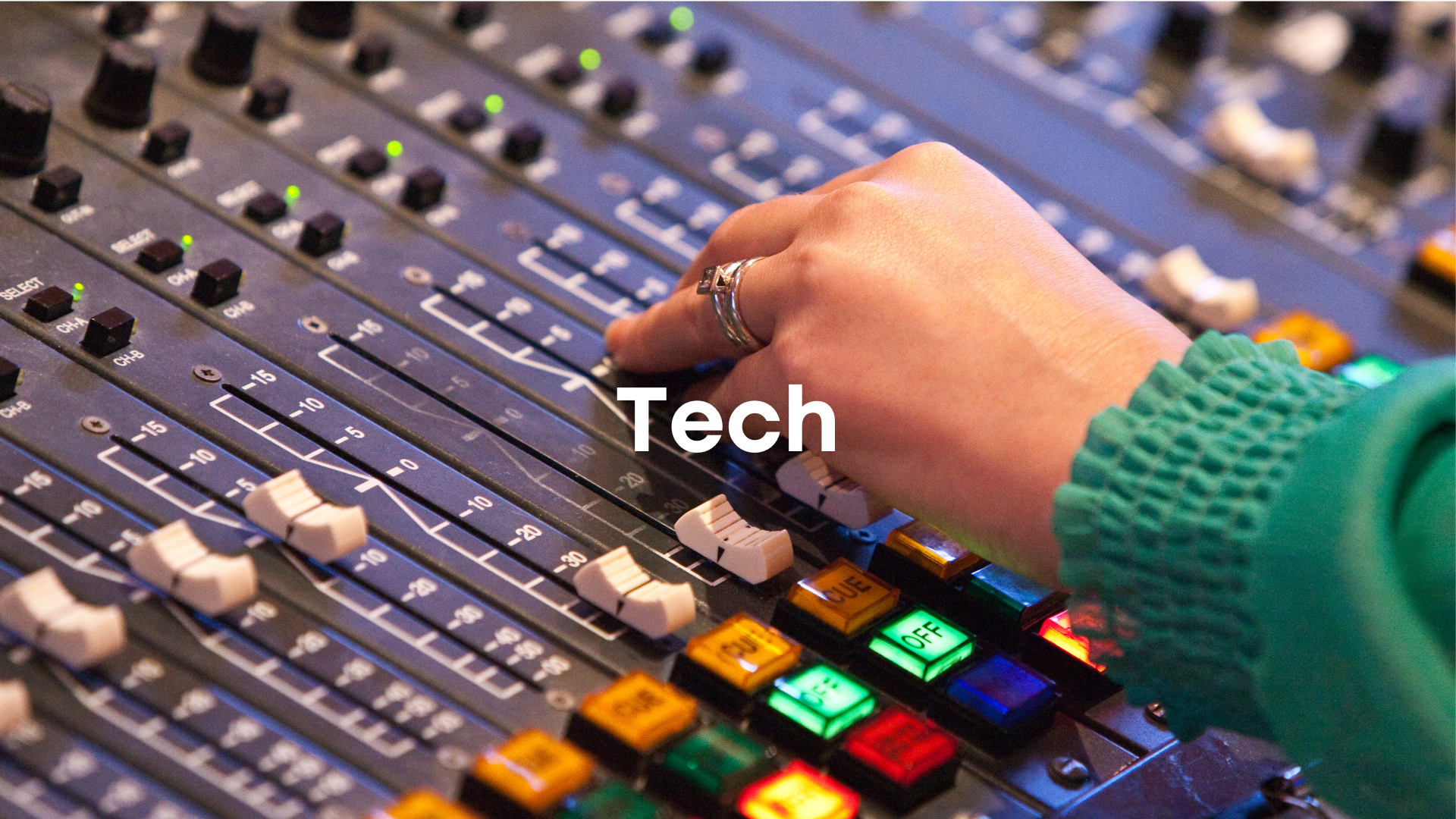 Close-up of a person's hand adjusting controls on a professional audio mixing console, with a green jacket sleeve visible.