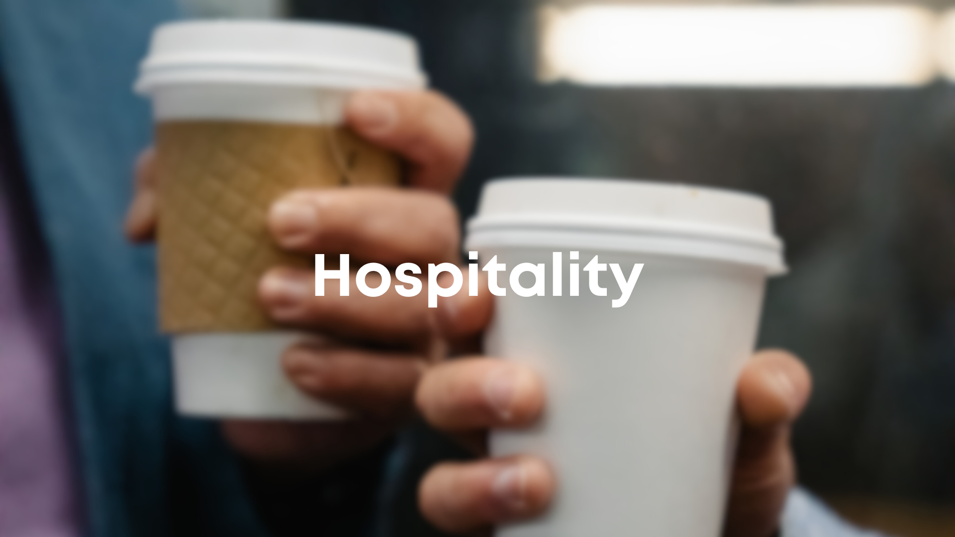 Close-up of two hands holding disposable coffee cups with white lids, one with a cardboard sleeve, on a blurred background. The word 'Hospitality' is overlaid on the image.