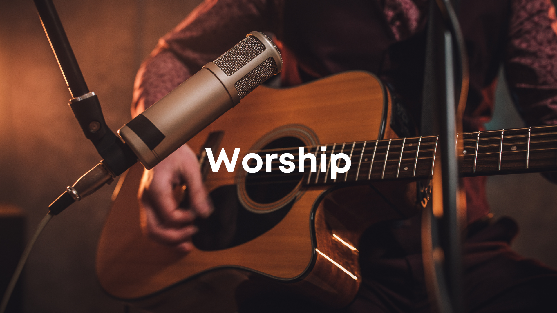 Person playing acoustic guitar with microphone in a worship setting.