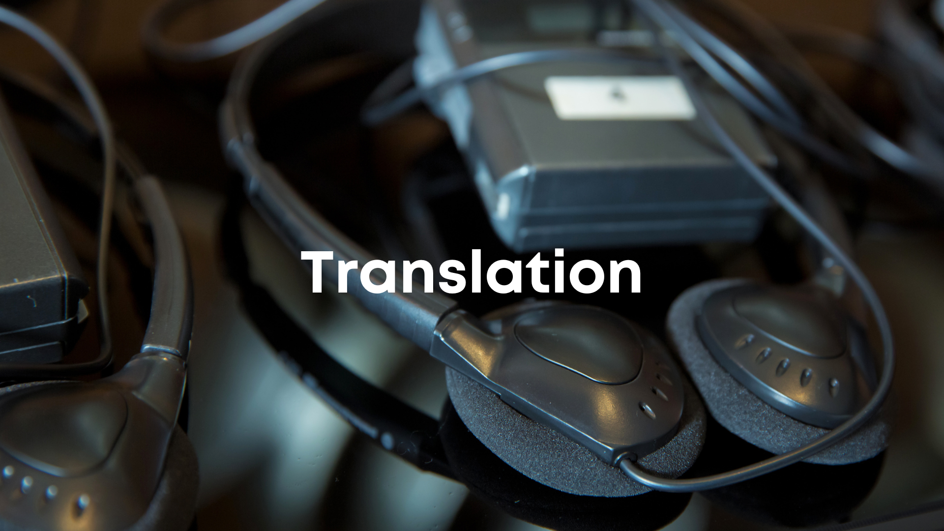 Close-up of a collection of headphones and audio equipment with the word 'Translation' overlaid.