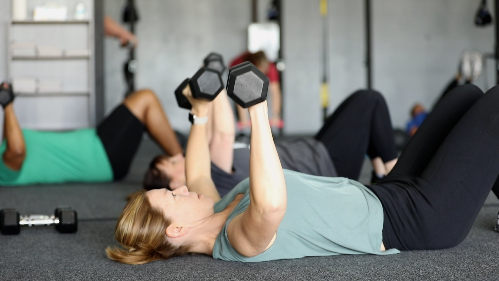 Group of people doing push-ups in a gym with dumbbells and kettlebells nearby
