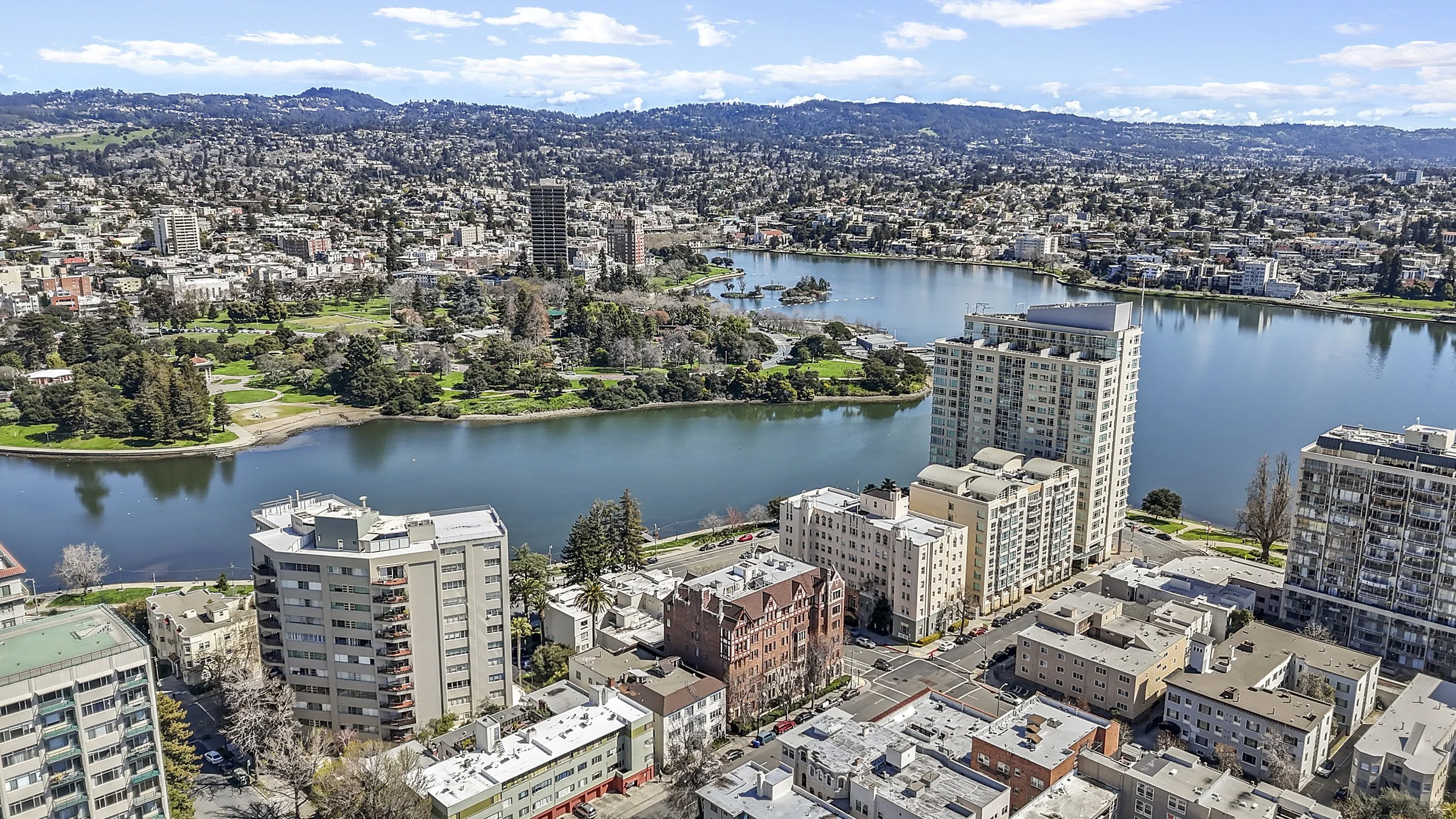 A cityscape view of San Francisco, California, with high-rise buildings, a large park, and a body of water, under a partly cloudy sky.