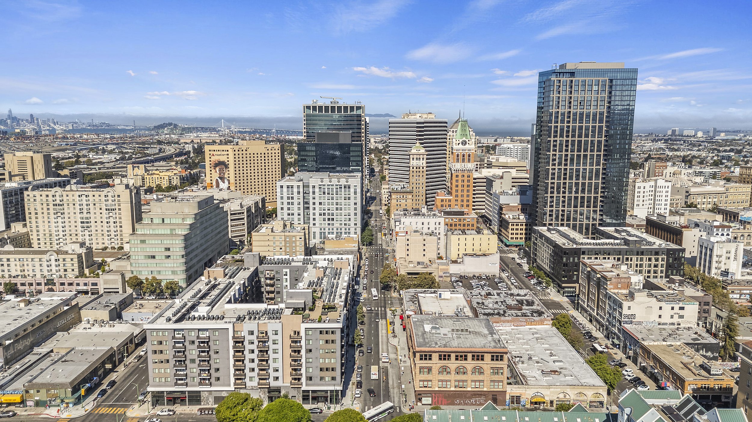 A city skyline with tall buildings, streets, and a bay with bridges in the background on a clear day.