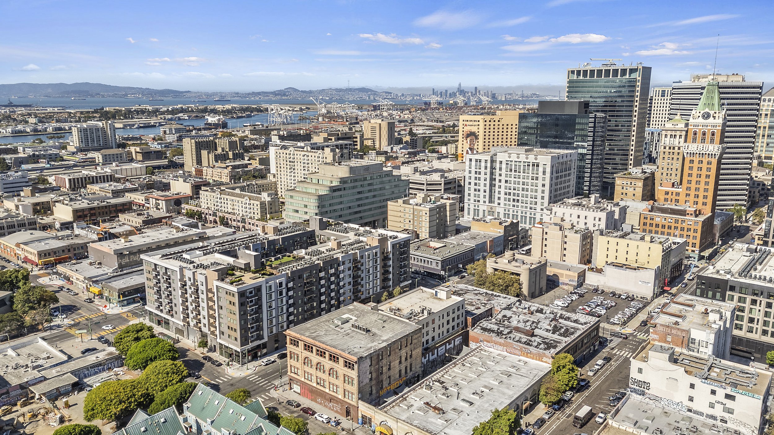 Aerial view of downtown cityscape with high-rise buildings, streets, a harbor with ships, and hills in the background.