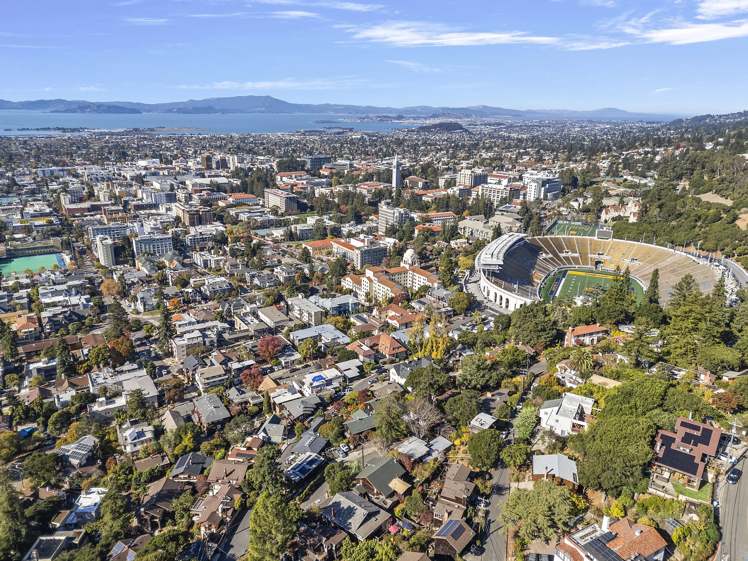 Aerial view of a city with numerous buildings, a football stadium, and a large body of water in the background.