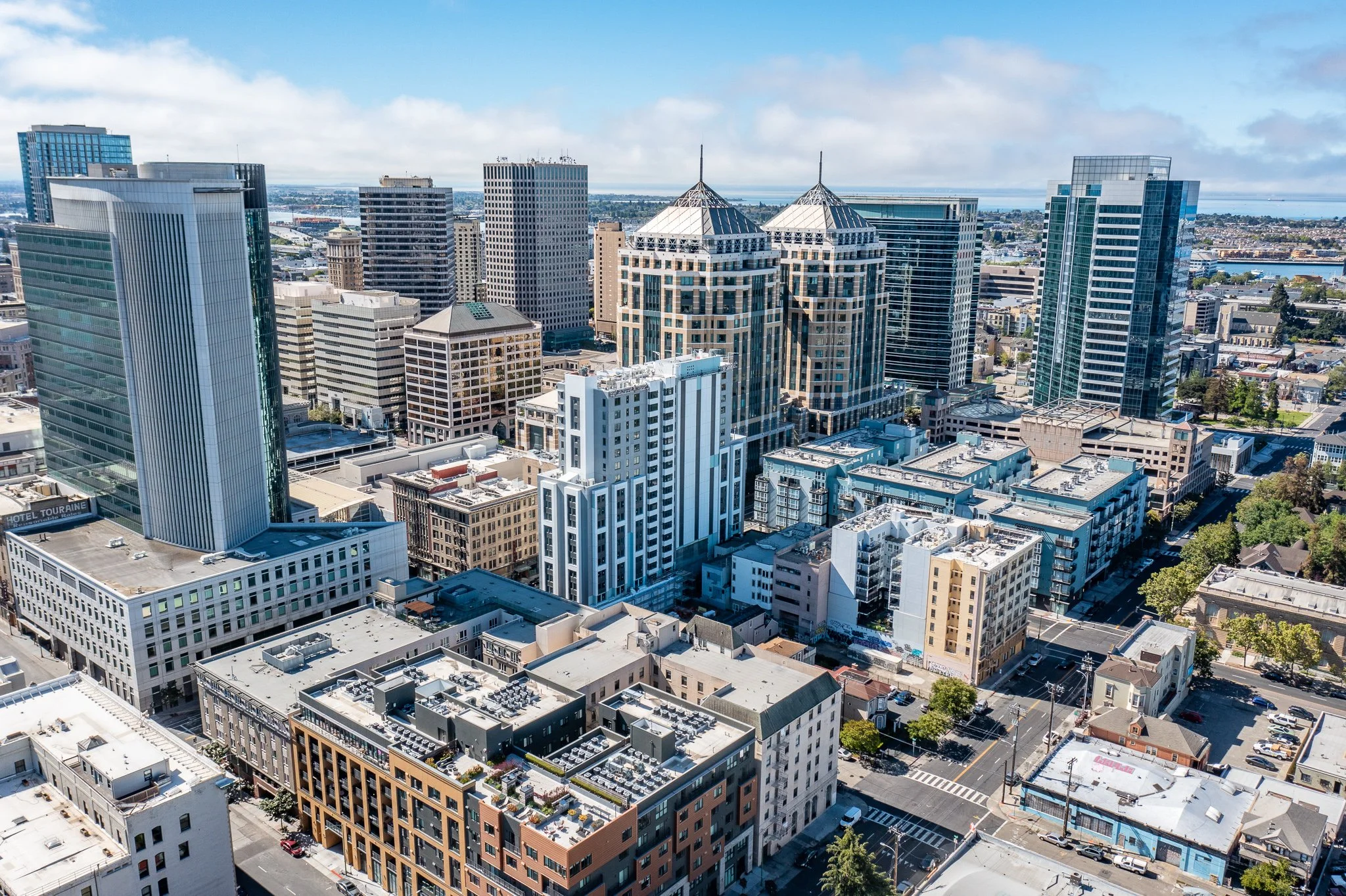 Aerial view of a city skyline with tall modern skyscrapers, some with glass facades, during daytime with a partly cloudy sky.