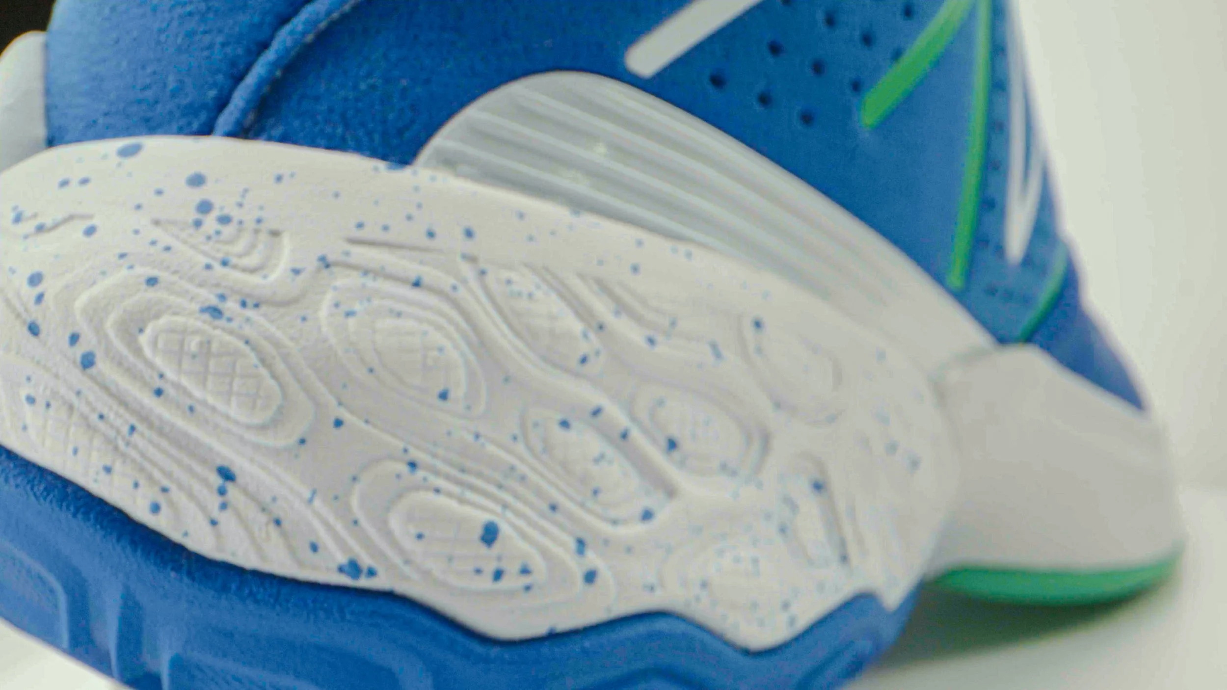Close-up of the sole of a running shoe, showing a textured white rubber pattern with blue speckles, with part of the blue upper visible.