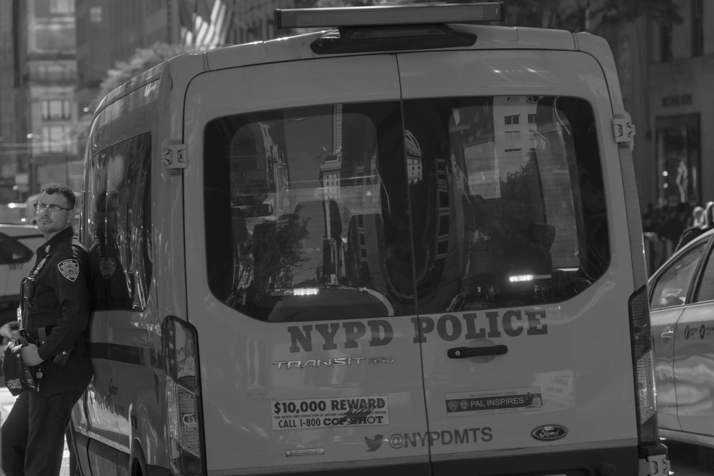 A police officer standing next to a NYPD police van on a city street.