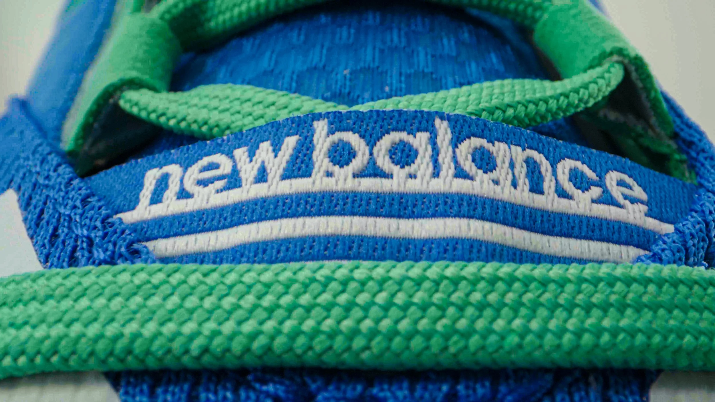 Close-up of a blue New Balance athletic shoe with green laces, showing the brand name embroidered on the tongue.