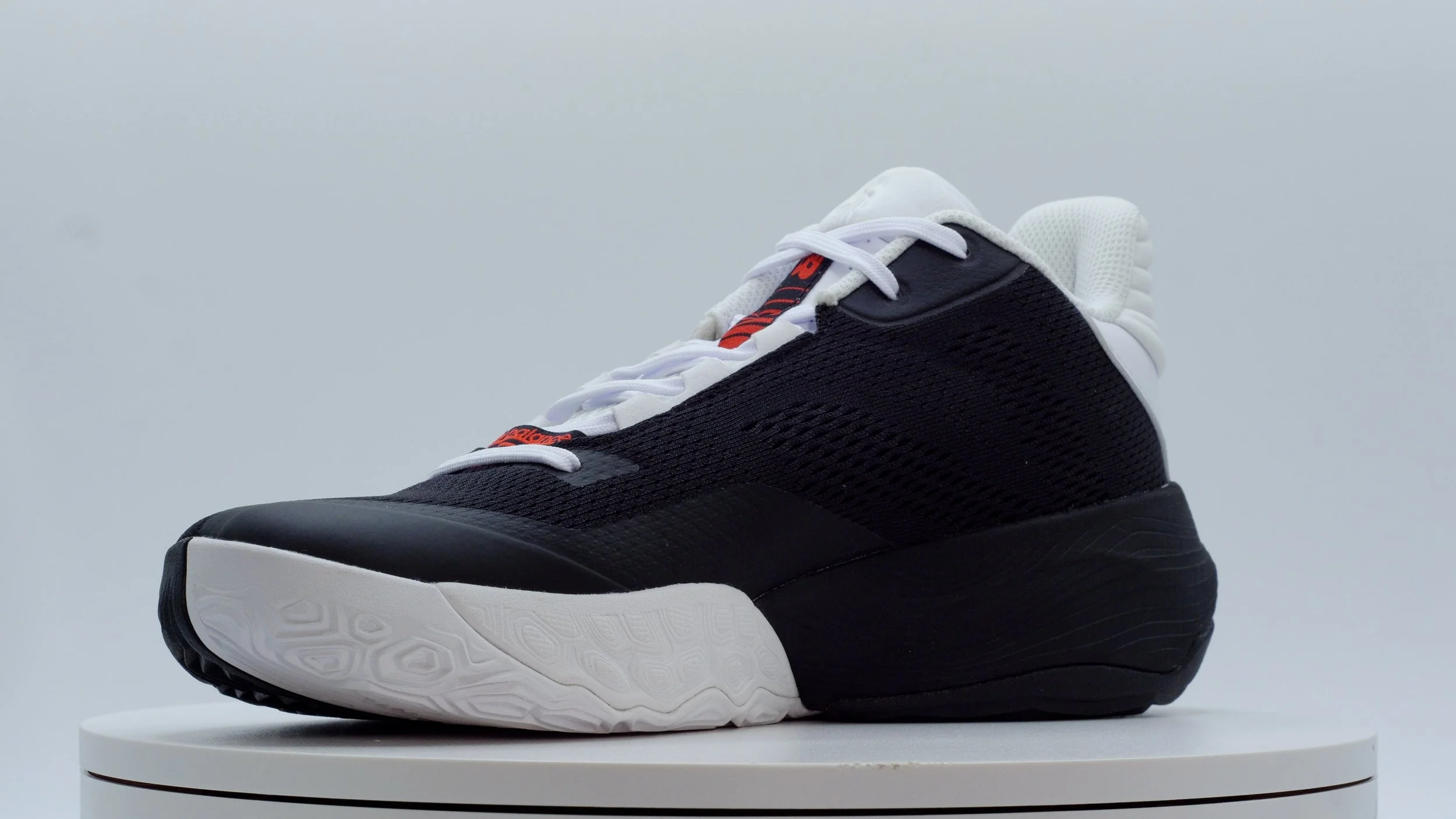 A black and white sneaker with a chunky sole, placed on a circular white platform against a plain light background.