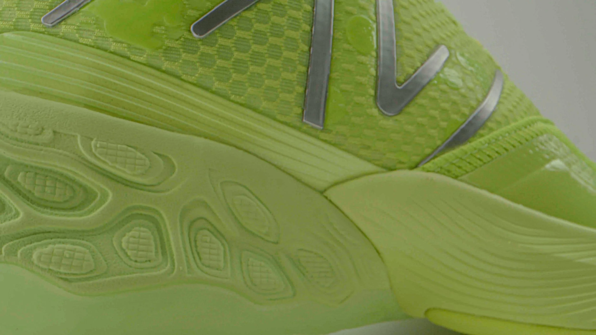 Close-up of a neon green athletic shoe, showing textured sole and part of the upper with metallic numbers.