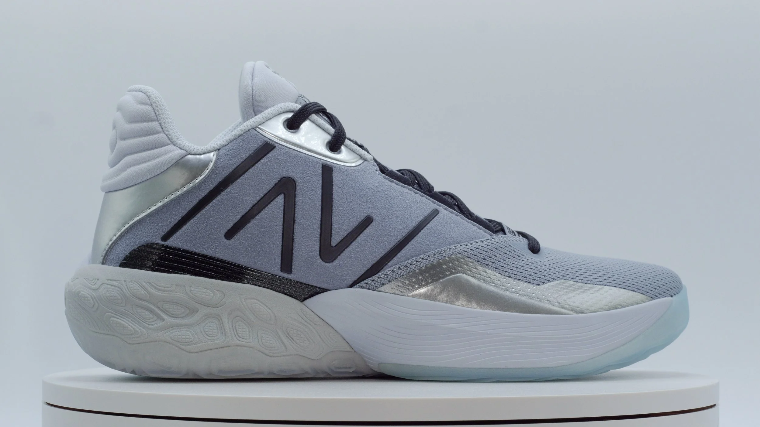 A modern athletic sneaker with a silver, gray, and black color scheme on a white display platform.