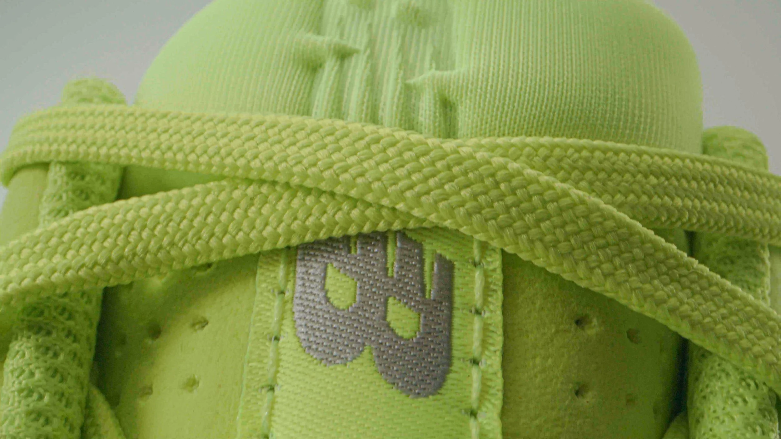 Close-up of a bright lime green sneaker with tied laces, showing a fabric label with a stylized alphanumeric logo.