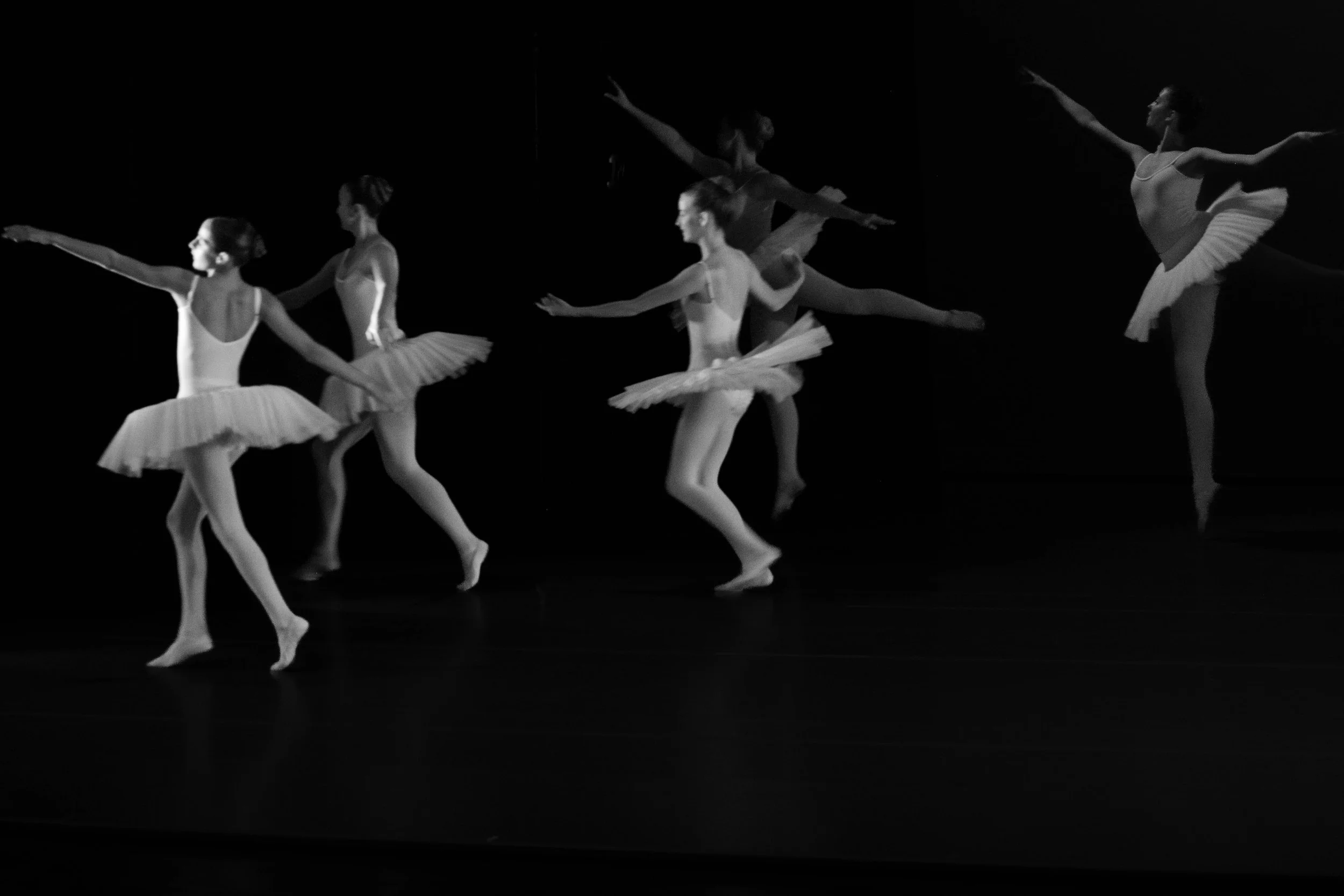 Black and white photo of five ballet dancers in tutu skirts performing on stage with dark background.