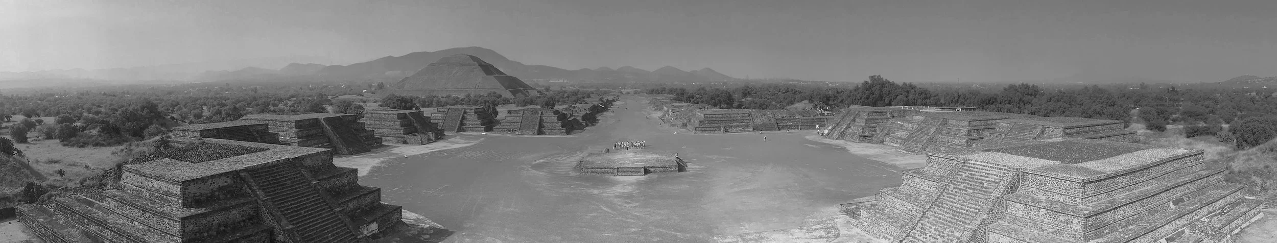 Ancient pyramid complex with large stepped pyramids, a central plaza, and a smaller circular structure, with a mountain in the background.