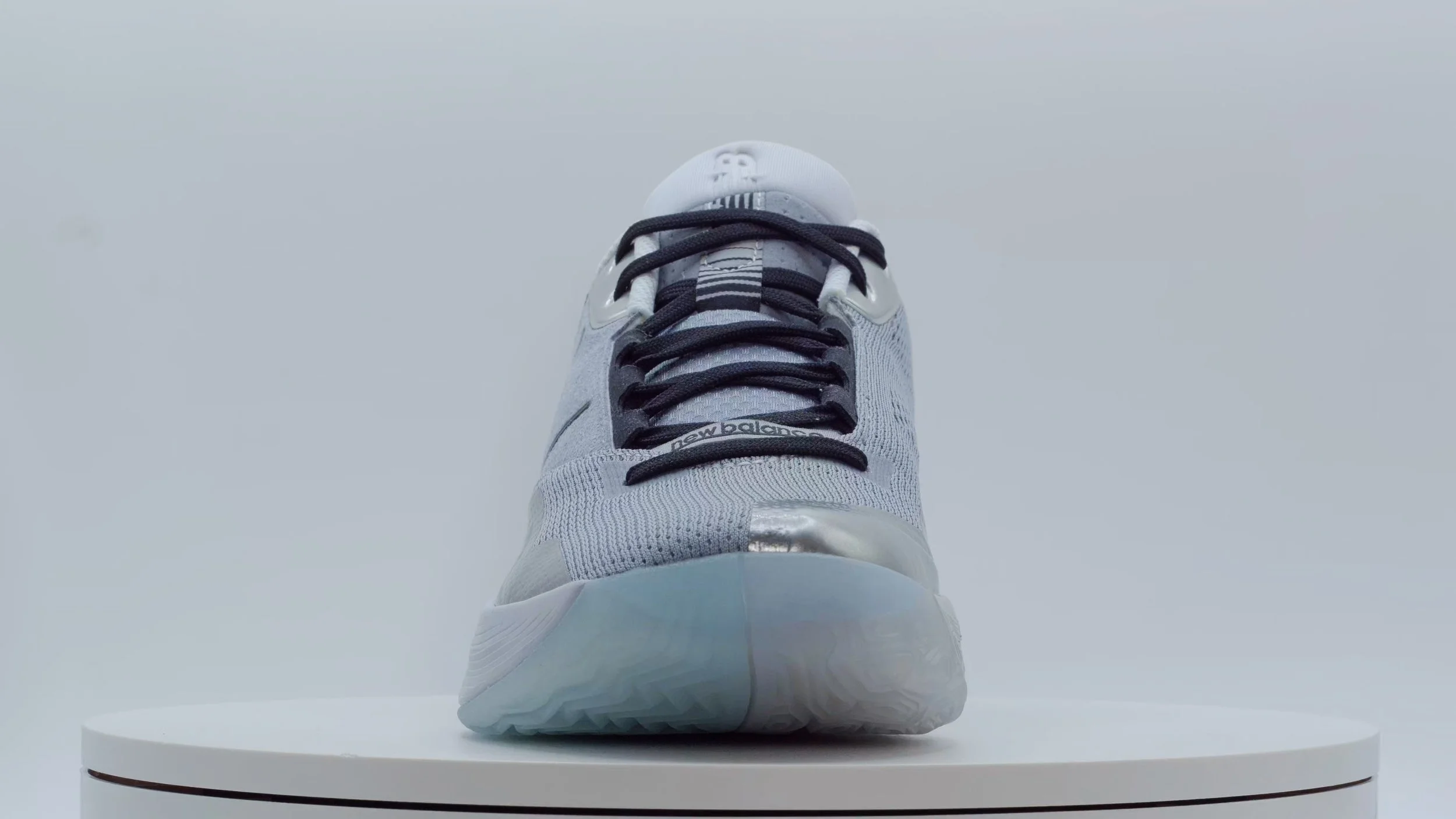 Front view of a white and grey New Balance sneaker on a white pedestal.