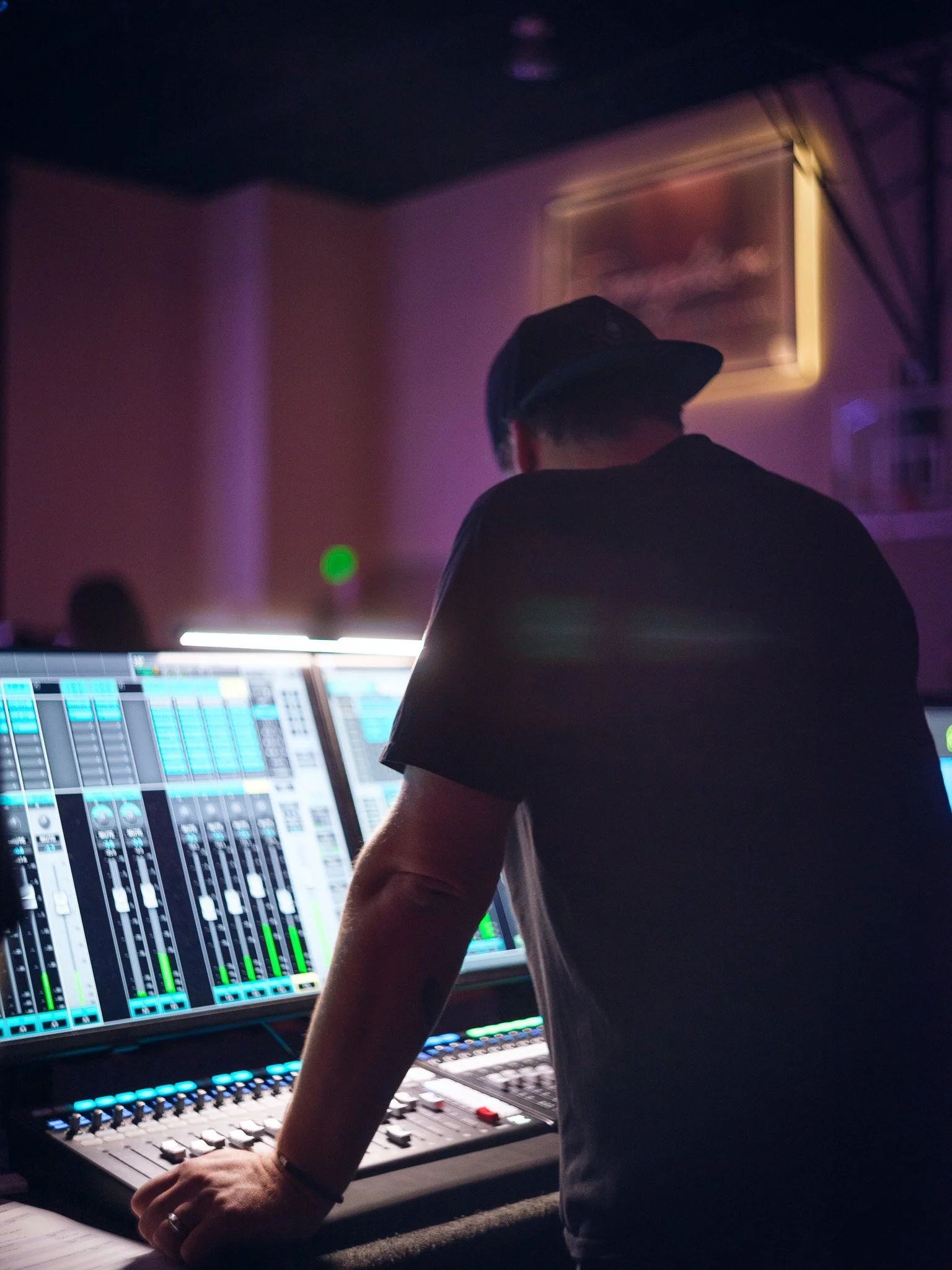A man operating a sound mixing console at a live event with people standing in the background.
