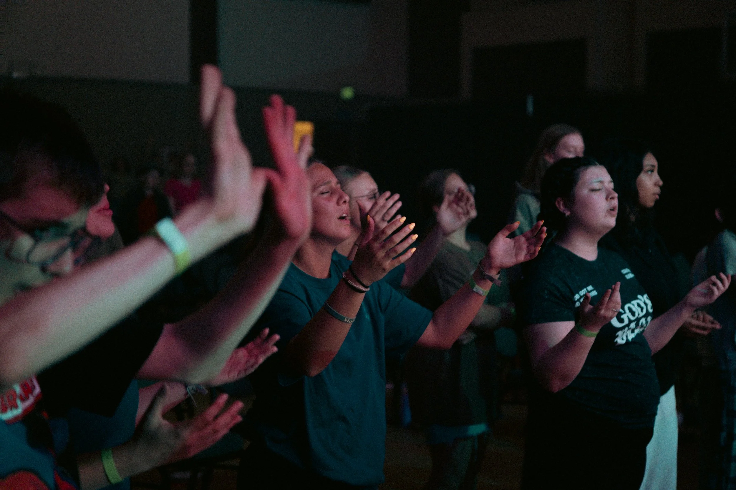 Audience members at a live event, with some raising their hands and others with their eyes closed, appearing engaged and emotional.