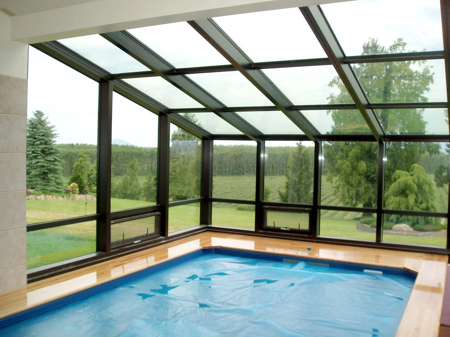 Indoor pool area with large glass windows and a view of green trees and lawn outside.