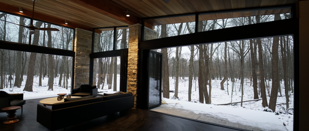 Modern living room with large floor-to-ceiling windows overlooking a snowy forest landscape.