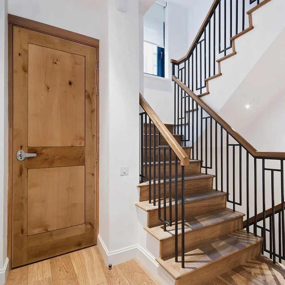 A wooden door next to a staircase with wooden steps and black metal railings in a modern home interior.