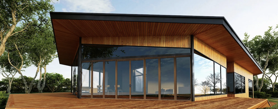 Modern house with large glass windows and a wooden exterior, surrounded by trees and a clear sky.