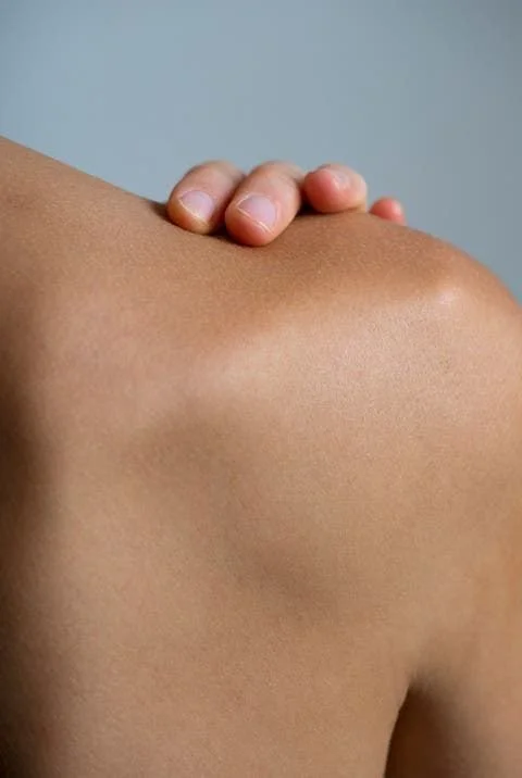 Close-up of a person's shoulder with gentle massage, showing smooth skin and a neutral background.