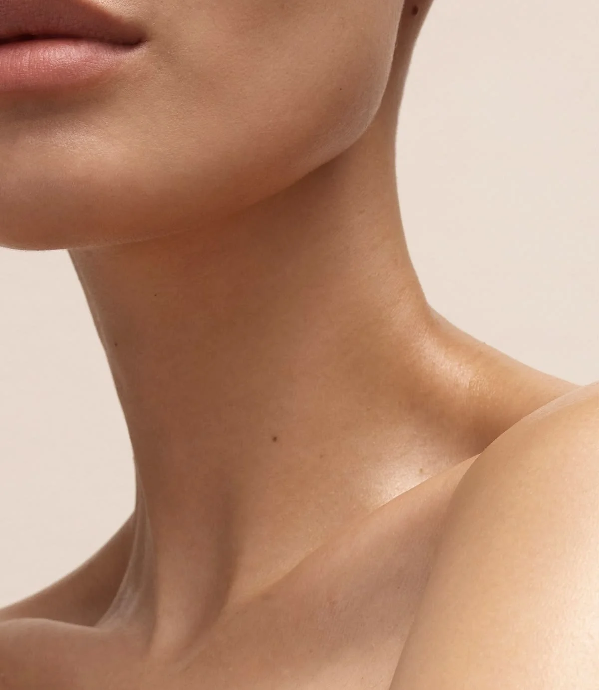 Close-up of a person's neck, shoulder, and lower face, showing smooth skin and subtle shadows.