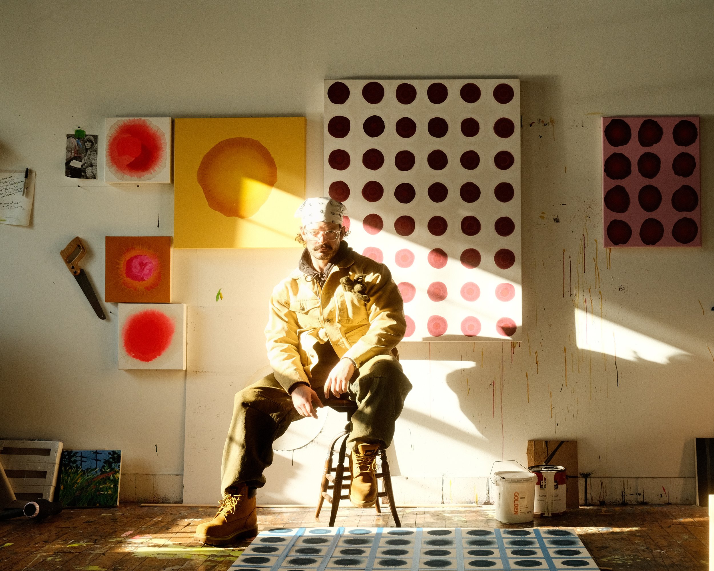 Picture of Patrick Walsh. A contemporary artist specializing in abstract, colorful paintings, sitting in his studio in Biddeford, Maine surrounded by his paintings.