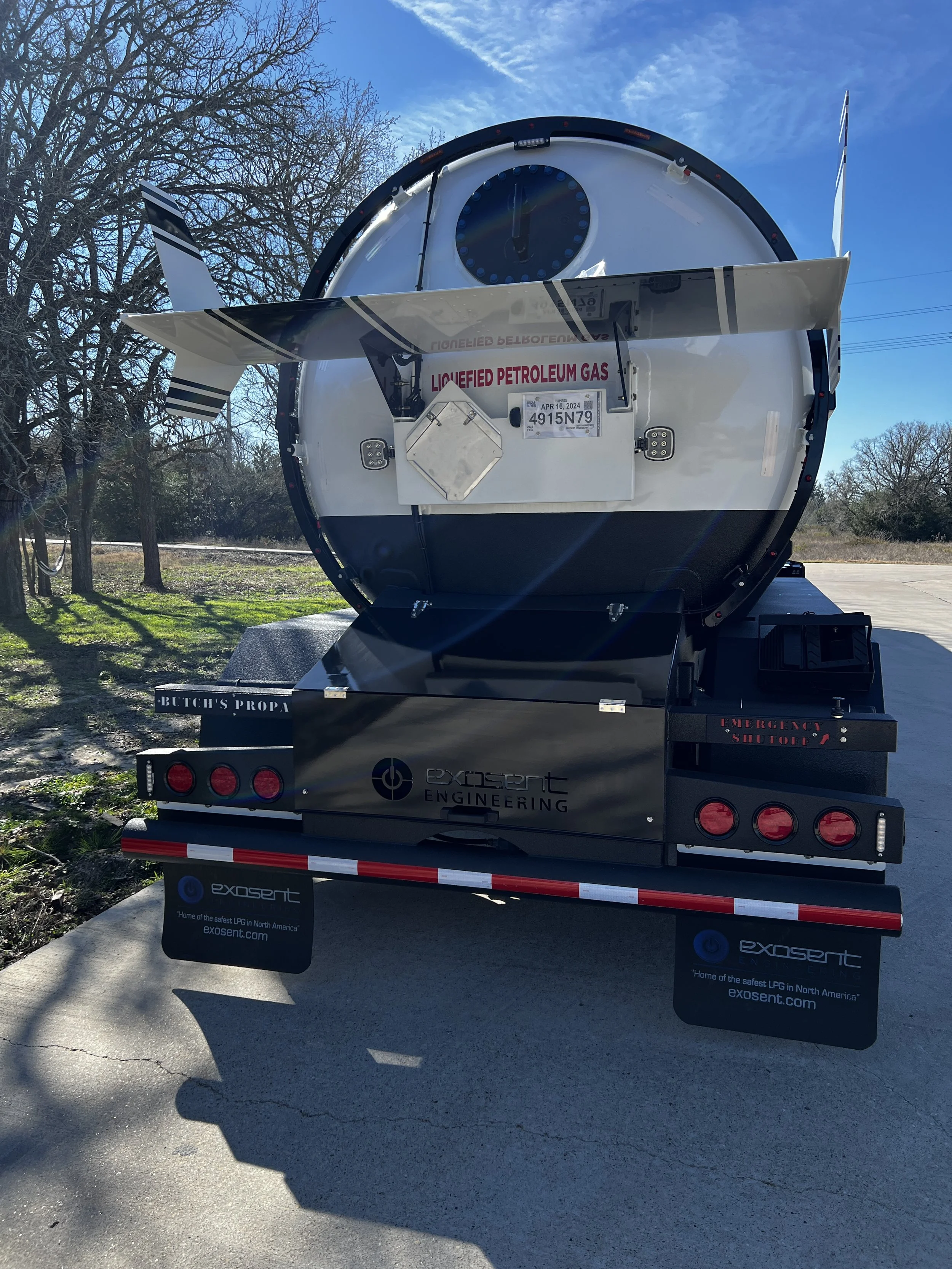 A fuel tanker truck labeled 'EXOSENT ENGINEERING' parked on a concrete surface, with leafless trees and a clear blue sky in the background.