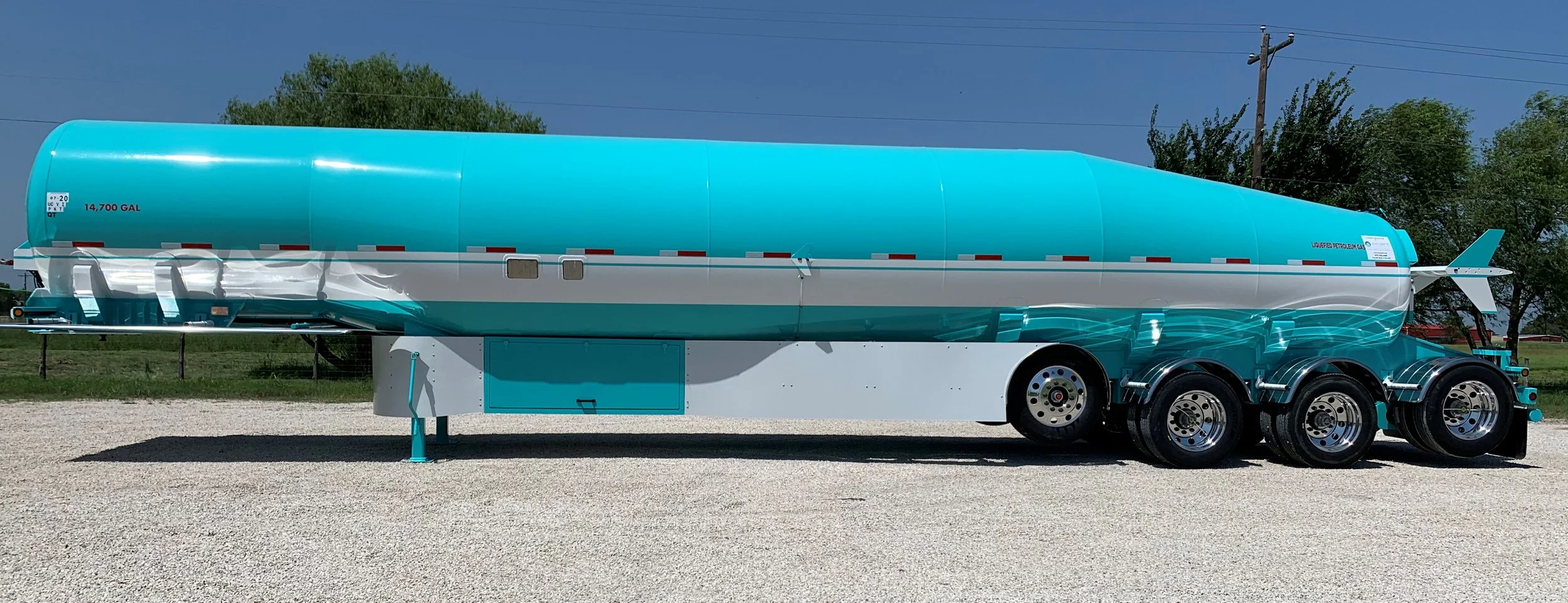 Bright turquoise rocket-shaped trailer on a gravel lot with trees and power lines in the background.