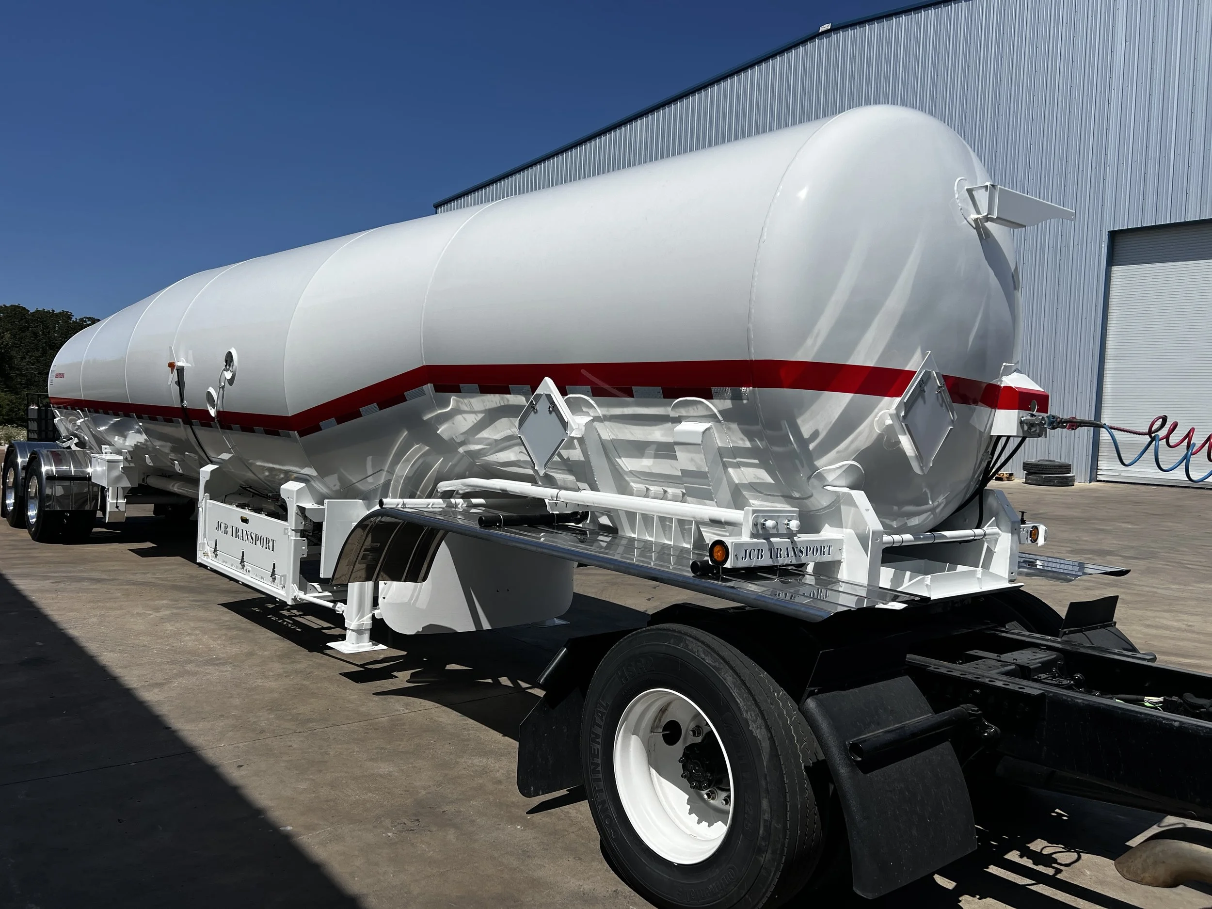 White tanker trailer with red stripe parked outside near a large blue warehouse