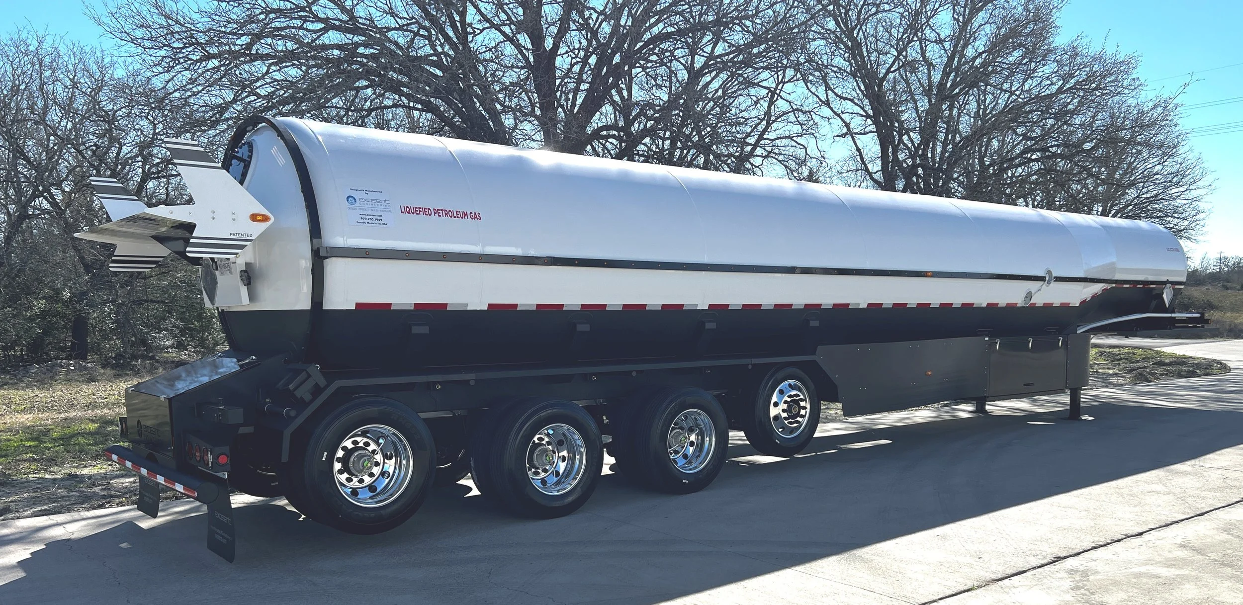A large tanker trailer transporting liquefied petroleum gas, parked on a concrete surface with trees in the background.