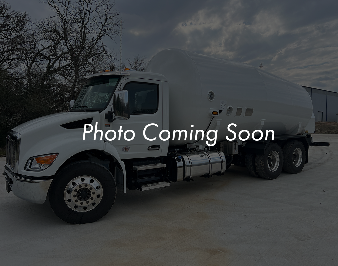 A white tanker truck parked outdoors under a cloudy sky with trees in the background.