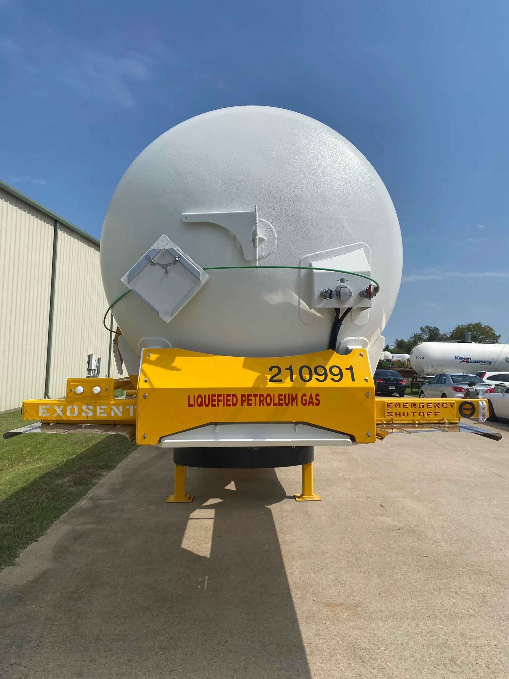 A liquefied petroleum gas tanker with a round white tank mounted on a yellow chassis labeled 'LIQUEFIED PETROLEUM GAS' and 'EMERGENCY SHUTOFF'.