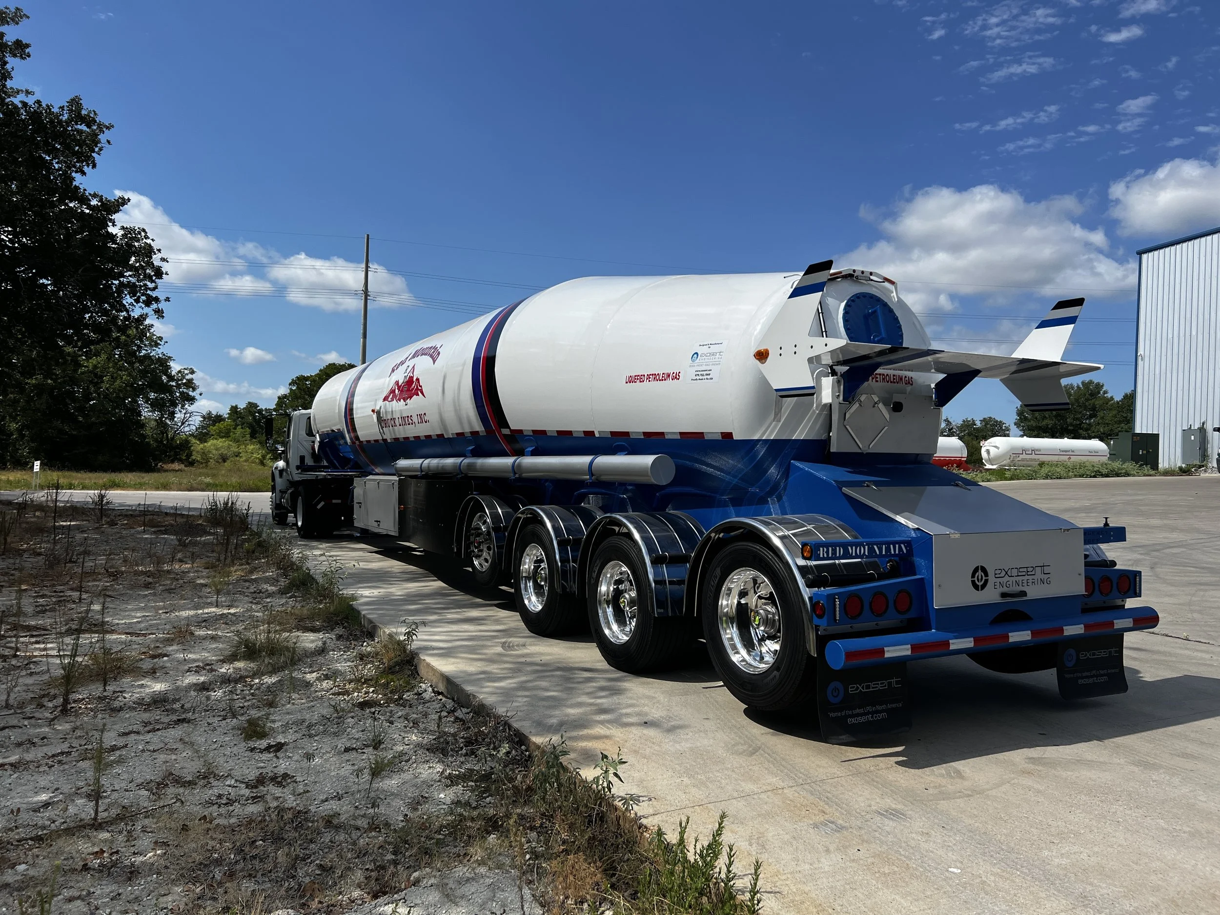 A fuel tanker truck parked on a concrete surface outdoors with a blue sky and some clouds in the background.
