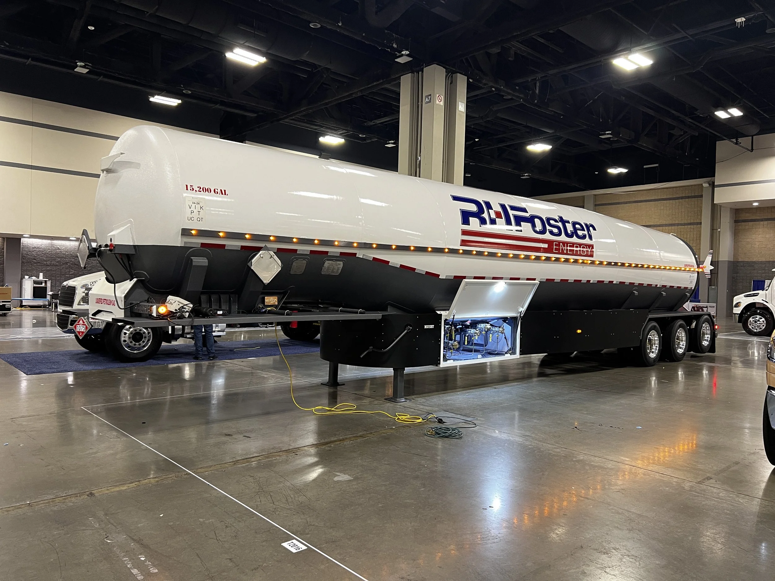 Large fuel tanker trailer displayed indoors at an exhibition, with the branding 'RHFoster Energy' on the side and a capacity of 15,200 gallons. The trailer is black and white with lights along the side.