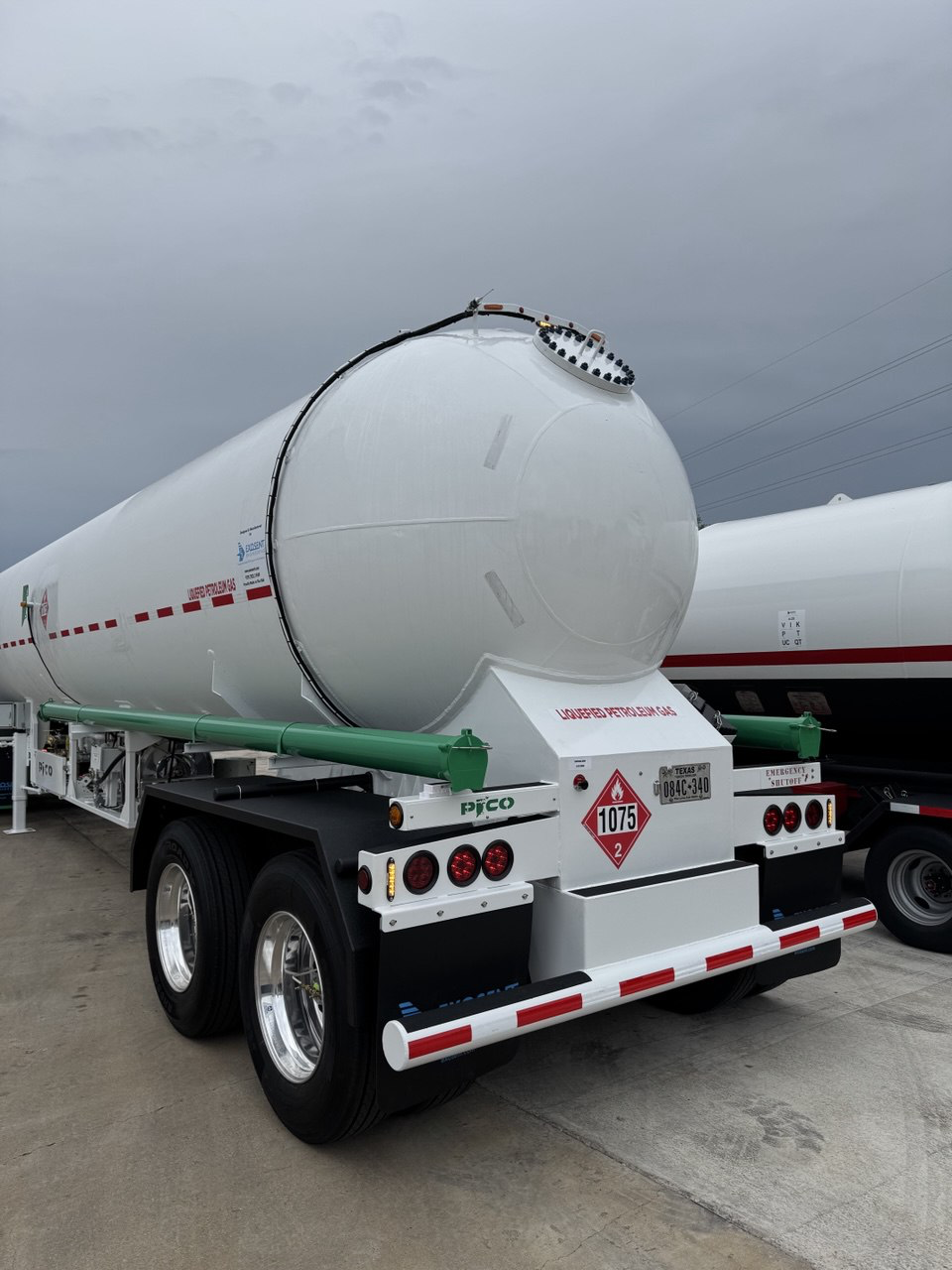 Ground tanker truck carrying liquefied petroleum gas with hazard labels, parked outdoors under cloudy sky.